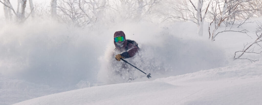 Skier carving through deep powder snow in Niseko Japan with birch trees and Mt. Yotei in the background during BSSC group ski trip